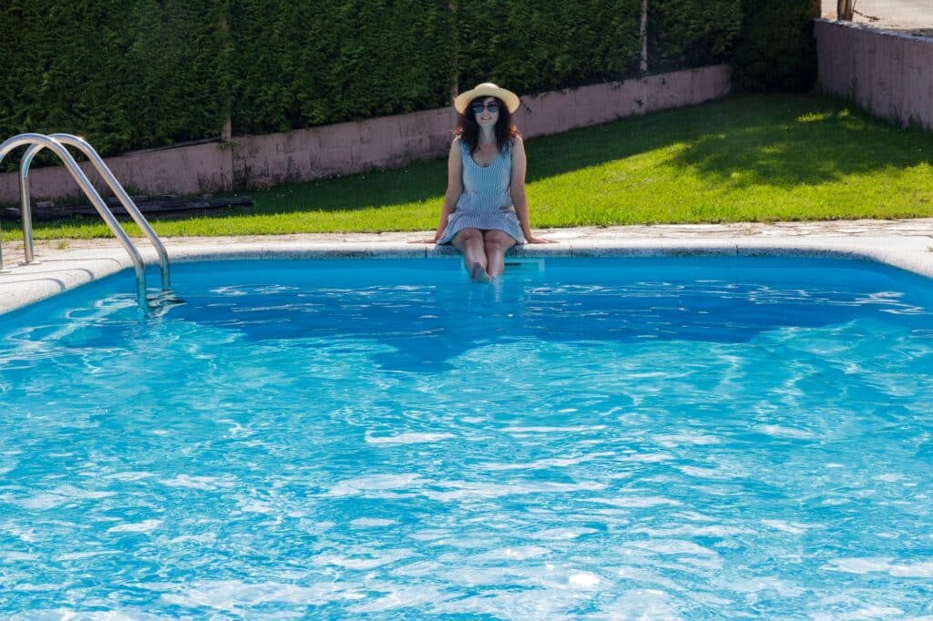Woman sitting on a pool with an straw , summertime, legs into the pool, backyard